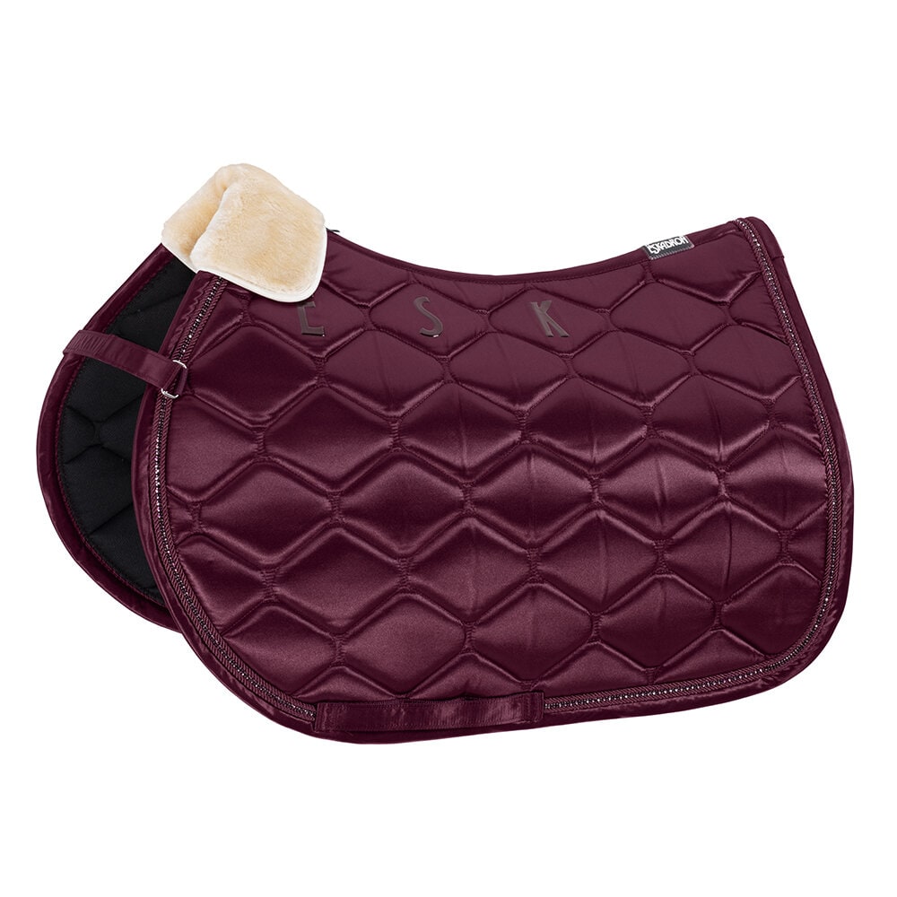 Ett quiltat schabrak i vinröd glansig färg med kristalldetaljer längs kanten och initialerna "ESK" i glänsande material över ryggen. Det har också ett krämvitt fårskinnsliknande material vid manken.